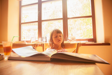 Little beautiful child girl reading with interest a book about world history of photography.