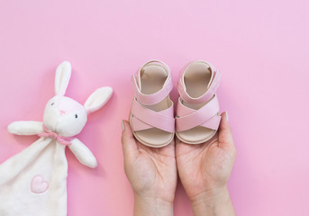 Hand holding baby shoes on a pink background