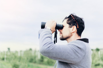 Portrait of young adventure man travelling with binoculars, watching landscape view outdoors. Young brunette man discover nature scenes. Travelling, discovering, vacation concept