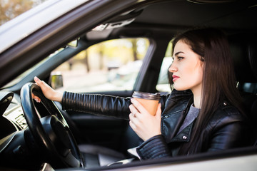 Fototapeta na wymiar Young beauty woman in formal wear driving a car and holding a cup of coffee