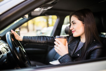 Fototapeta na wymiar Happy young woman with coffee to go driving her car in the morning