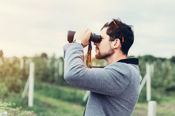 Portrait of young adventure man travelling with binoculars, watching landscape view outdoors. Young brunette man discover nature scenes. Travelling, discovering, vacation concept