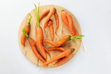 Ugly carrot on a round wooden board.  Ugly food concept, flat lay.