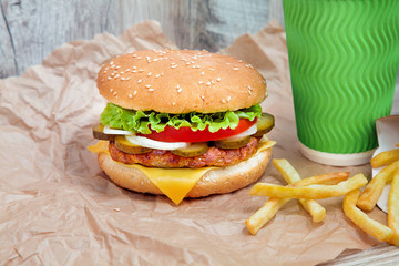 Close up view on burger with french fries on craft brown paper. Traditional fast food. fresh tasty cheeseburger with lettuce, tomato, cheese and cucumber. Copy space for design. Unhealthy food. Fat