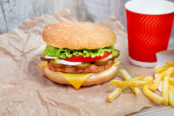 Close up view on burger with french fries on craft brown paper. Traditional fast food. fresh tasty cheeseburger with lettuce, tomato, cheese and cucumber. Copy space for design. Unhealthy food. Fat