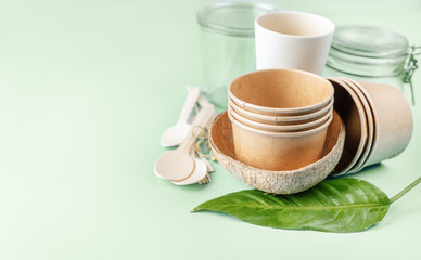 Eco tableware on light green background. Paper and bamboo cups, bag and wooden cutlery.