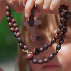 Close up little child girl seeing on cross of rosary. Selective focus on cross.