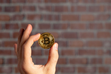 man hand holding a physical bitcoin in front of a brick wall