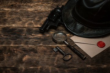 Obraz premium Top secret envelope, gun, leather hat, key and magnifying glass on a wooden table of detective agent table background.