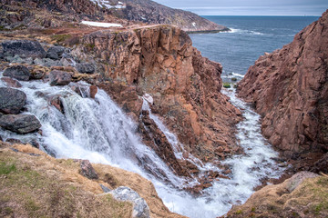 Stormy waters of the northern waterfall in a rocky gorge on the shores of the cold sea, Teriberka, Russia
