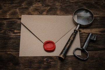 Old envelope with a sealing wax stamp, rusty key and a magnifying glass on a brown wooden table...
