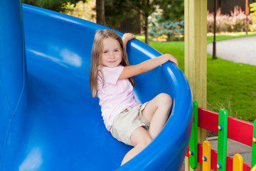 Fototapeta na wymiar Cute little girl having fun on a playground outdoors on a sunny summer day. Child on plastic slide. Fun activity for kid. active sport leisure for kids