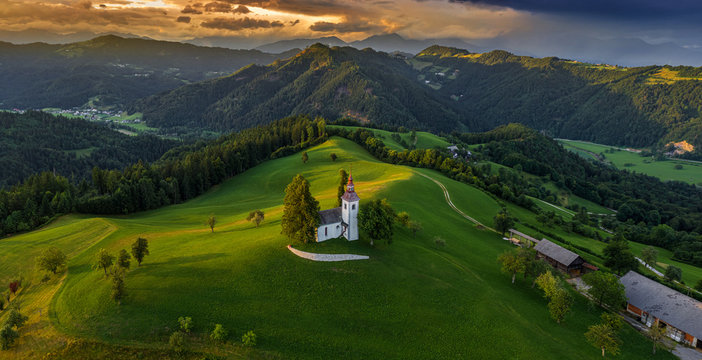 Fototapeta Skofja Loka, Slovenia - Aerial panoramic view of the beautiful hilltop church of Sveti Tomaz (Saint Thomas) with amazing golden sunset and the Julian Alps at background at summer time
