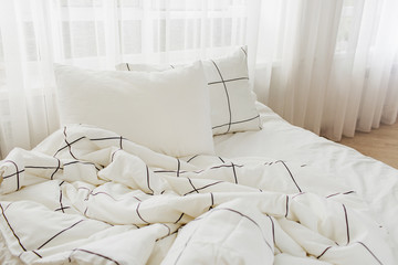 Fototapeta na wymiar White bedding sheets with striped blanket and pillow. Messy bed.