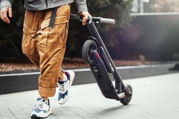 Close up of man holding electric kick scooter while going for a walk at street.
