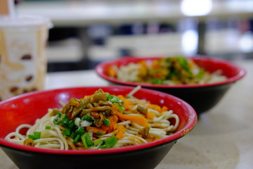 close up hot dry noodles with sesame paste in red bowls. Popular traditional breakfast of Wuhan Hubei China. Blur background