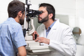 male doctor ophthalmologist is checking the eye vision of handsome young man in modern clinic. Doctor and patient in ophthalmology clinic .