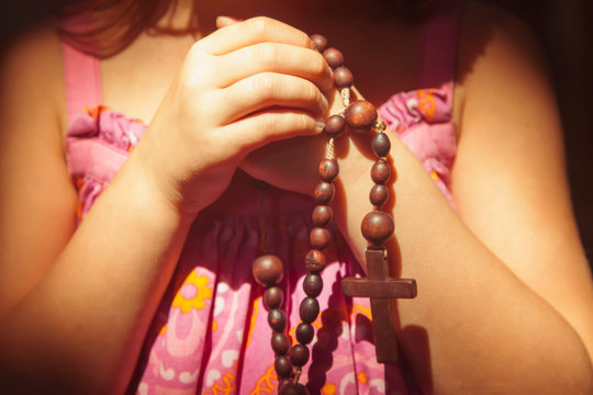 Hands of child girl with rosary. She is praying to God.