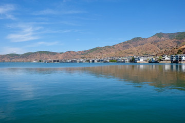 mountains and inn houses along the blue Erhai lake in Shuanglang Yunnan China. Symmetrical reflection in peaceful water. Sunny blue sky white clouds. Famous tourist attraction