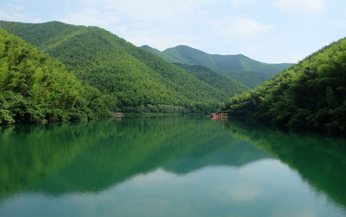 Fototapeta na wymiar green mountains and symetrical reflection in peaceful lake. blue sunny sky and white cloud. South Hill Bamboo Sea in China Jiangsu. wide angle