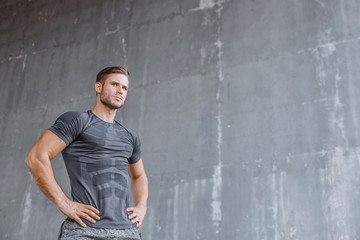 Muscular model in fashion sportswear on urban gray background. Portrait of brutal  strong guy with a modern trendy hairstyle. Sports young man working out outdoor.