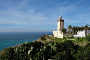 Fototapeta na wymiar In Morocco Tangier white lighthouse near blue ocean. Sunny clouds skyline . Green cactus foreground. Cape Malabata with a lighthouse. promontory at the entrance to the Strait of Gibraltar