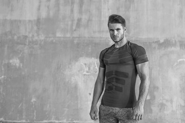 Black and white. Muscular model in fashion sportswear on urban gray background. Portrait of brutal strong guy with a modern trendy hairstyle. Sports young man working out outdoor.