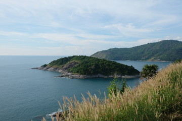 Prom thep cape island in sea south of Phuket Island Thailand. Blue sunny cloudy sky and wide ocean water. brown reeds as foreground