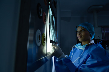 Female surgeon holding x-ray against light box in operation theater