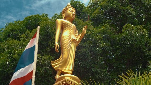 Beautiful female golden budah statue outside a typical temple in Thailand with thai flag flying alongside