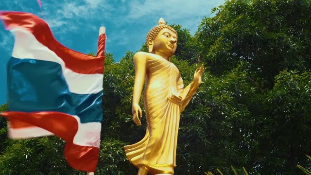 Beautiful female golden budah statue outside a typical temple in Thailand with thai flag flying alongside