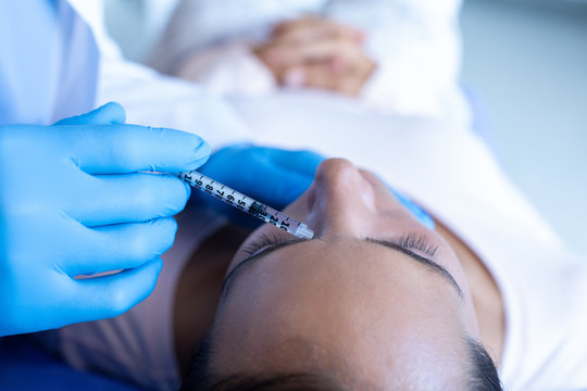 Surgeon giving injection to face of female patient