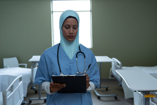 Female doctor in hijab writing in clipboard in the ward