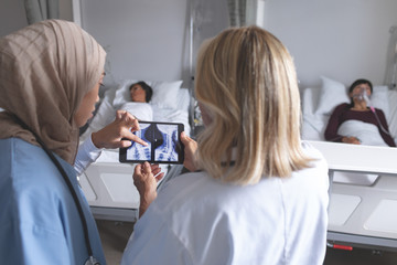 Female doctors discussing over x-ray report on digital tablet in the ward at hospital