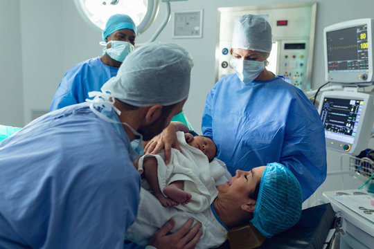 Couple With Surgeons Holding Their Newborn Baby In Operating Room
