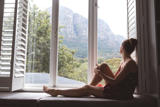 Woman sitting on window seat and looking outside in bedroom at home