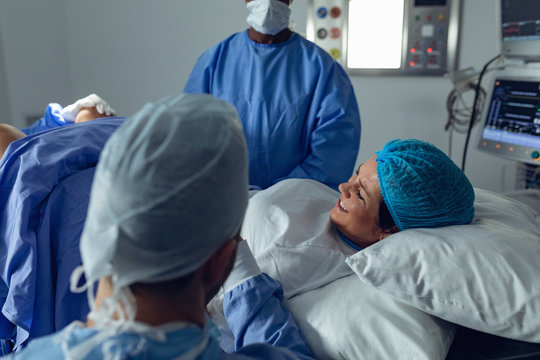 Surgeons examining pregnant woman during delivery while man holding her hand in operating room