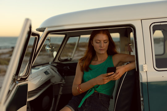 Beautiful woman using mobile phone on front seat of camper van at beach