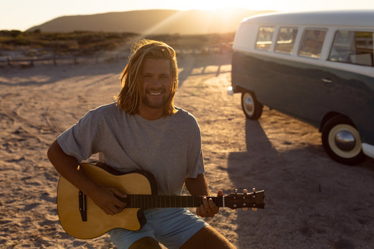 Happy young man playing guitar near camper van at beach
