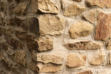 Background in the form of a corner of a stone wall of a light brown rubble, frontal side in the sun, lateral in the shade