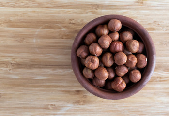 Obraz premium Hazelnuts are poured into a brown clay bowl on a light brown background, top view