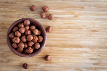Hazelnuts in a violet ceramic bowl on a light brown background, on the right an empty space, top view