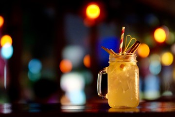 Close up a jar looking glass of beverage with ice cubes on table. Defocused colorful lights background. Bar and restaurant concept