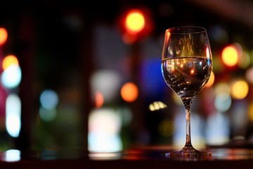 Close up a glass of wine on table. Blurred colorful lights background. Low angle. Bar and restaurant concept