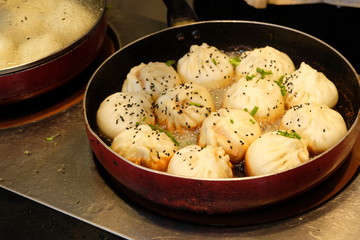 close up white fried buns in a rounded pan under light on cooking bench . Pan-Fried buns stuffed with pork is a popular traditional Chinese food. 