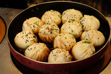 close up white fried buns in a rounded pan under light on cooking bench . Pan-Fried buns stuffed with pork is a popular traditional Chinese food. 