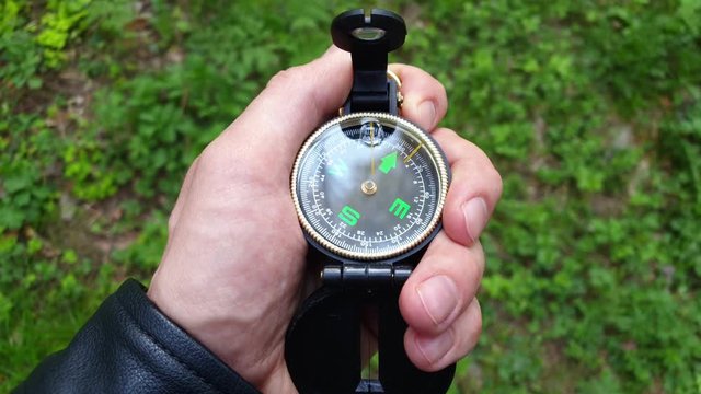 A man holds a compass and points it to the north, POV, does not know how to use.