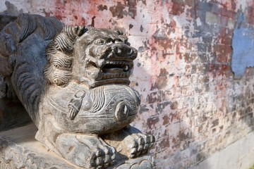close up one grey traditional Chinese stone lion in front of blurred mottled wall under sunshine