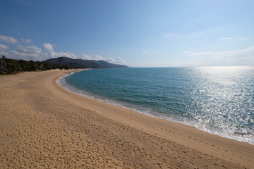extended empty sand beach and coastline. nobody. sunny blue sky white cloud. blue sea with sunshine reflection. wide angle