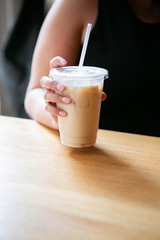 Woman holding Iced Chai Latte in To Go Cup on Table, Coffee on Wooden Bar in Cafe, Close up photo
